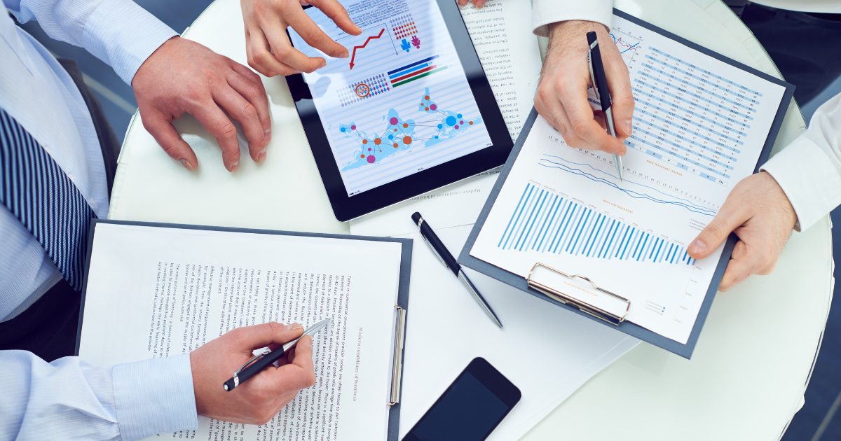 Close-up of business professionals analyzing data on printed reports and a digital tablet during a team meeting.