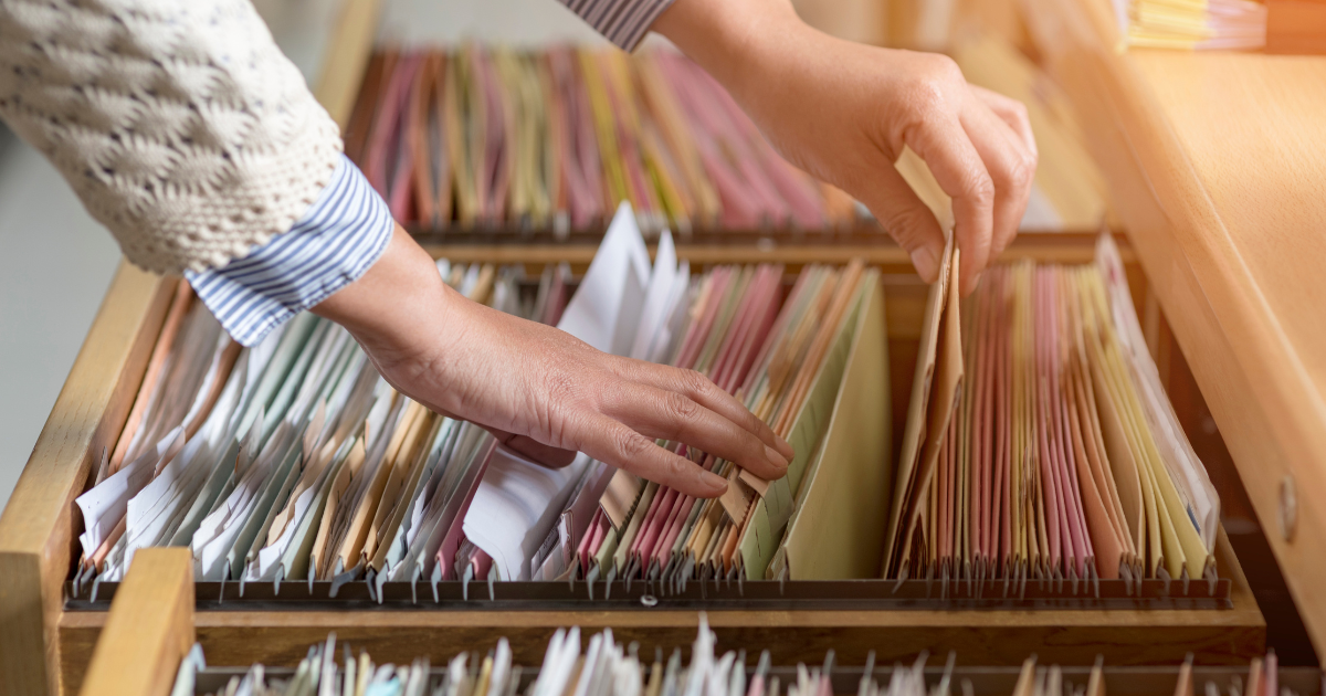 Person sorting through paper files in a wooden filing cabinet, representing manual document search.