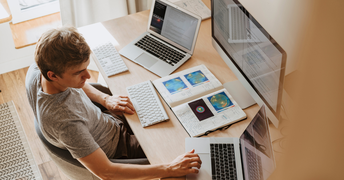 Young professional working at a desk with multiple devices and notebooks, managing data and multitasking remotely.