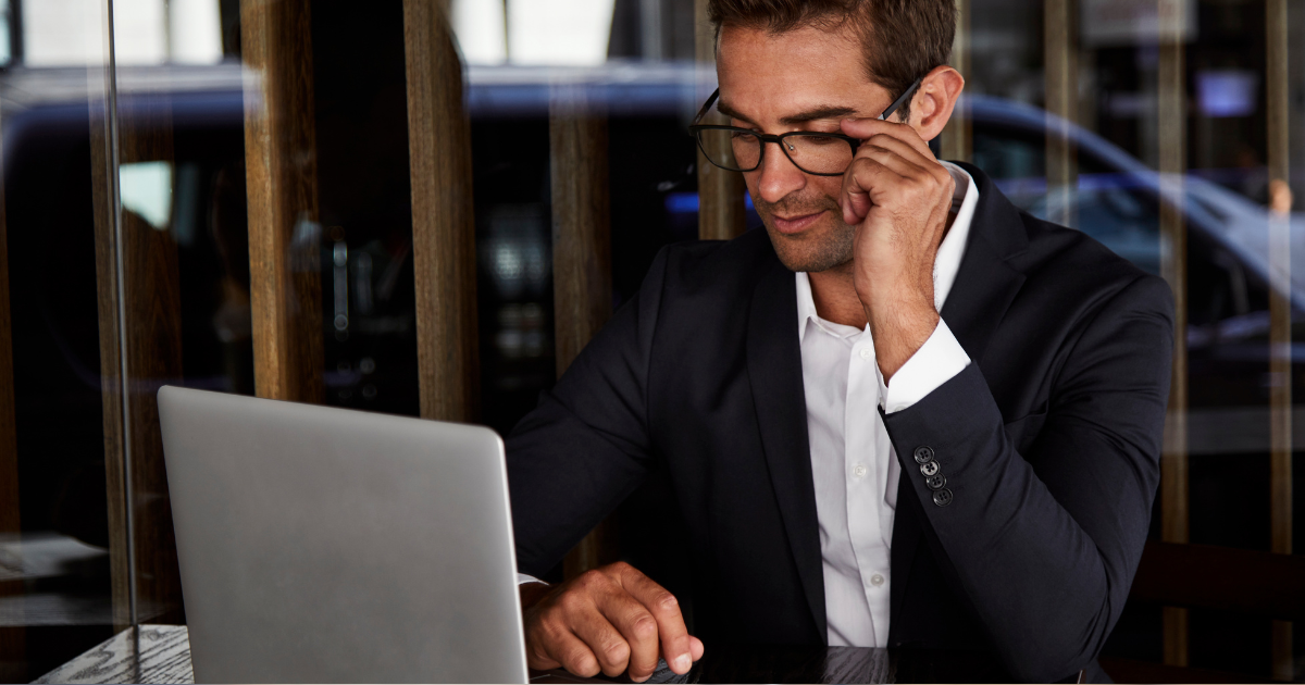 Business professional in a suit working on a laptop at a modern café or office setting.
