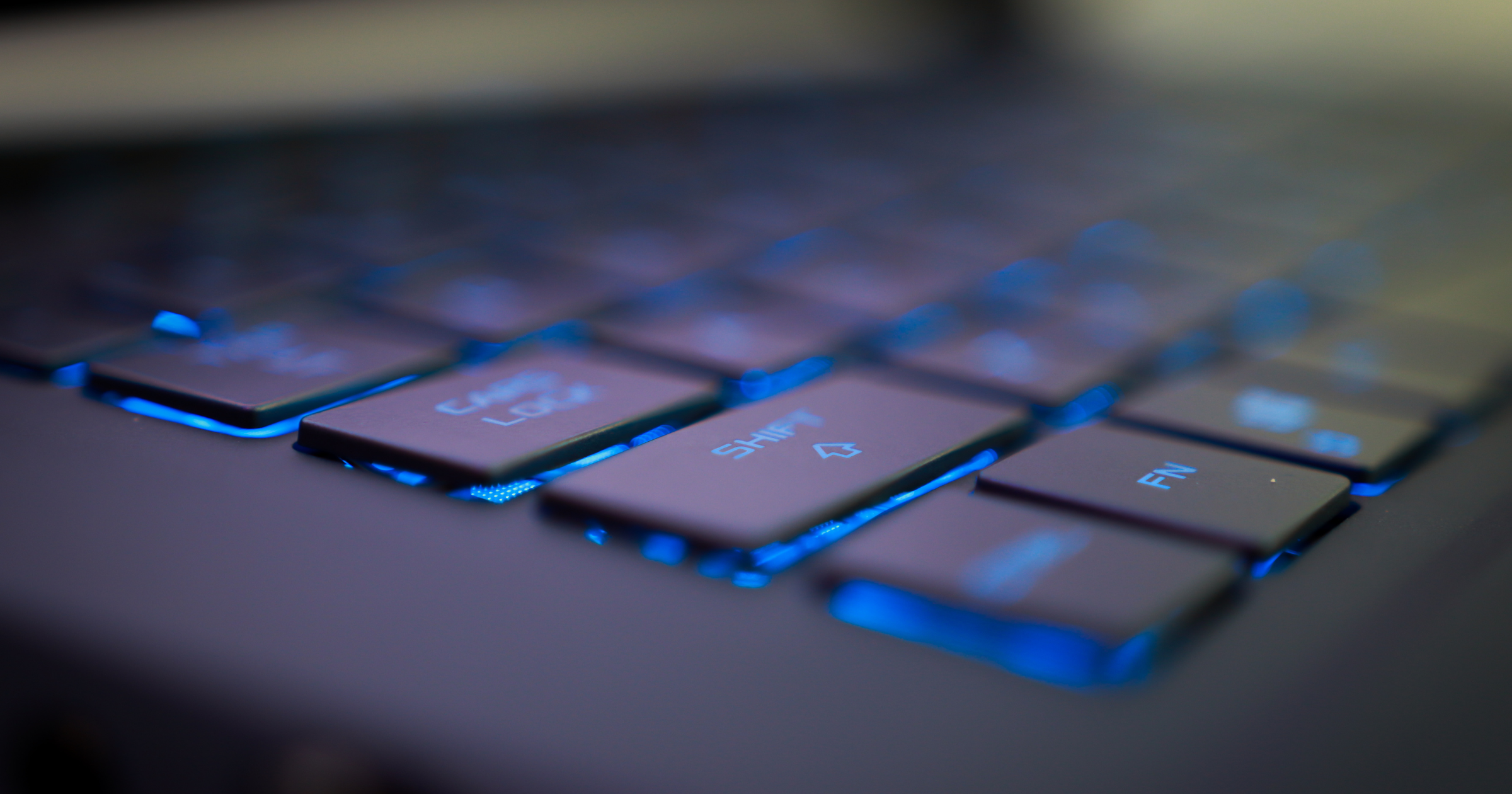 Close-up view of a backlit laptop keyboard with glowing blue light beneath the keys.